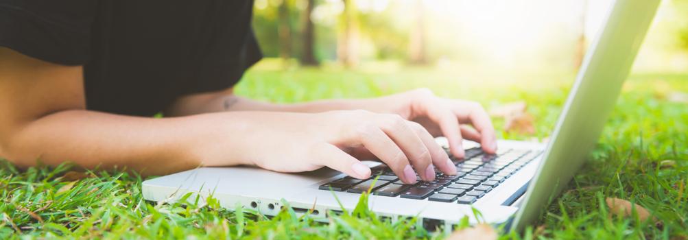 Person laying in the grass typing on a laptop computer